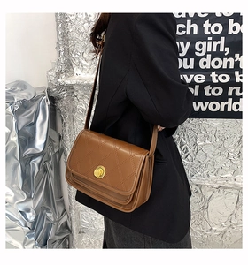 Detail view of brown quilted crossbody bag with golden circular metal lock and strap