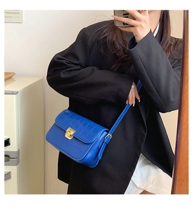 Detail of blue crocodile pattern flap bag with golden metal lock and thin shoulder strap