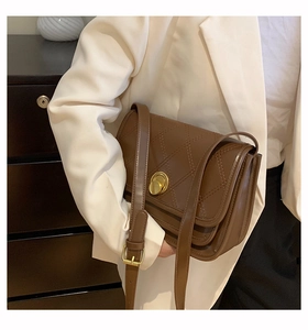 Detail of a brown leather shoulder bag with quilted stitching and metal twist lock