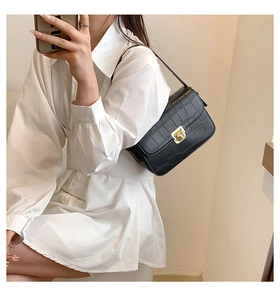 Model wearing a black crocodile pattern crossbody bag with a golden turn-lock closure