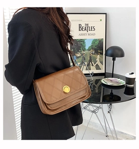 Close-up of a brown quilted crossbody bag with a large gold metal buckle on a model