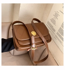 Close-up of brown quilted crossbody bag featuring a golden round buckle and premium texture