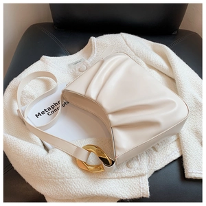 Detailed view of beige pleated shoulder bag with elegant gold chain on a black seat