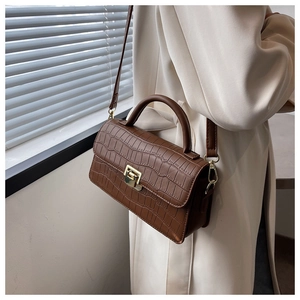 Vista dettagliata della borsa marrone con texture coccodrillo e fibbia dorata su trench