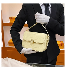 Close-up of yellow crocodile pattern handbag held by a gloved hand in luxury setting