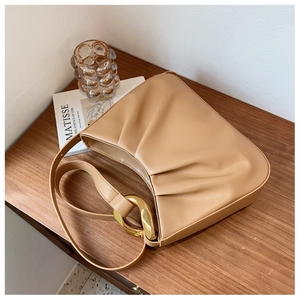 Detailed close-up of light brown pleated cloud bag with golden metal ring buckle on wood