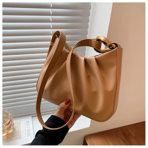 Close-up of pleated camel bucket bag with chunky gold chain strap in soft lighting