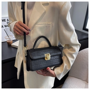 Dettaglio della borsa in pelle nera a coccodrillo con chiusura dorata su un blazer