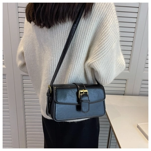 Close-up of black patent leather shoulder bag with a gold buckle and slim strap