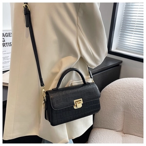 Dettaglio borsa nera texture coccodrillo con chiusura dorata su sfondo blazer bianco