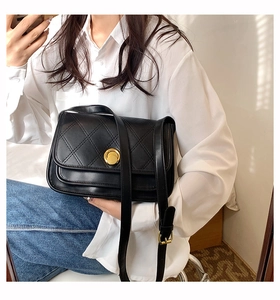 Close-up of black quilted leather shoulder bag with round golden twist lock on a model