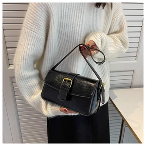 Detail of black glossy shoulder bag with gold buckle on a white knit sweater background