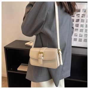 Detail of cream white leather shoulder bag with gold metal buckle on a grey blazer outfit