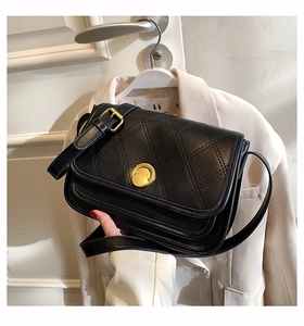Detail of black diamond-quilted crossbody bag with golden round metal twist lock clasp