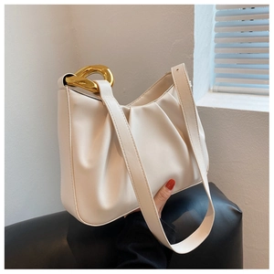 Detail of beige pleated cloud bag with chunky gold chain handle held against light shadow