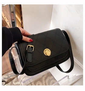 Detail of black quilted crossbody bag featuring a golden circular twist lock and leather strap