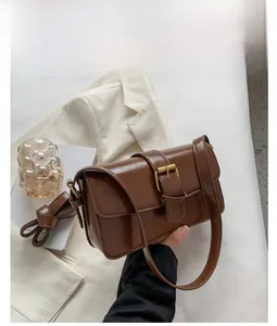 Detail of coffee brown faux leather vintage shoulder bag with gold buckle on white suit