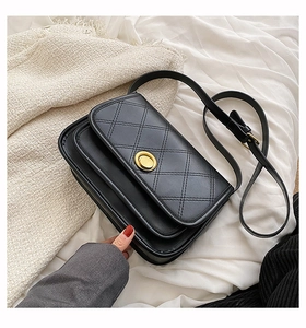 Detail of black quilted crossbody bag featuring a golden round metal clasp and strap