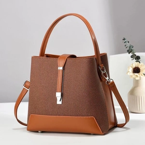 Detail of a brown bucket bag with textured fabric, leather trim, and silver metal clasp