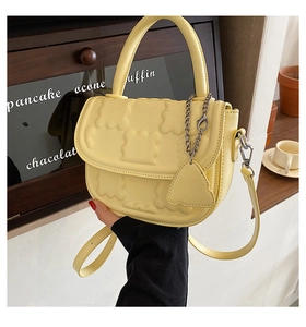 Detail of light yellow handbag with embossed bear texture and heart chain charm