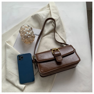 Detail of dark brown vintage baguette bag with oil-wax leather texture and gold buckle