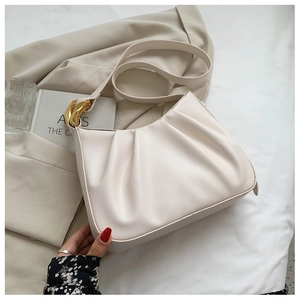 Detail of cream pleated shoulder bag featuring gold chain link hardware and smooth zipper