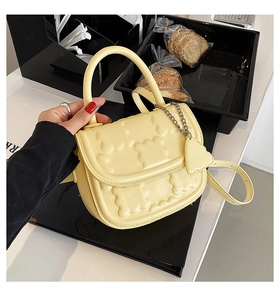 Detail of yellow quilted crossbody bag with heart pendant on a black book prop