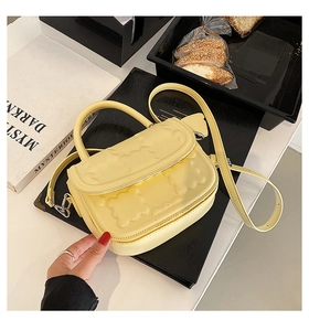 Detail of light yellow handbag featuring 3D embossed texture and top handle with shoulder strap