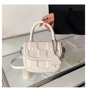 Detail of off-white quilted handbag with wave pattern and decorative metal chain pendant