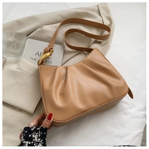 Detail of light brown ruched bucket bag with gold metal rings and leather texture