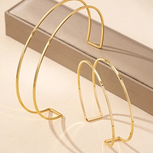 Detail of minimalist gold-finish geometric cuff bracelets on a textured background