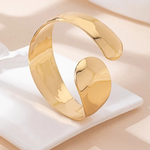 Detailed view of wide gold cuff bracelet featuring a polished mirror surface and open design