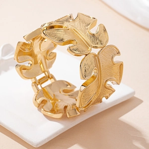 Macro detail of golden irregular monstera leaf bangle with delicate veining on white tray