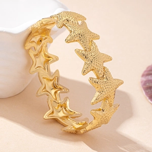 Detail of gold starfish bangle with textured metal surface on beach shells