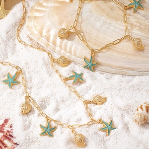 Nahaufnahme von goldenem Seestern und Muschel an einer Büroklammerkette auf Sand
