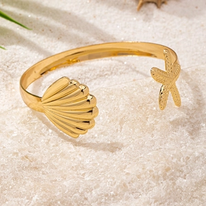 Detail of golden starfish and seashell cuff bracelet on sand with palm leaf shadows