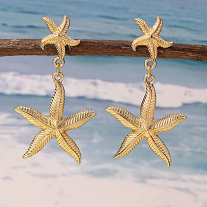Golden starfish dangle earrings with detailed texture displayed on a beach branch