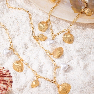 Golden sea shell and heart pearl charms necklace laid on white beach sand
