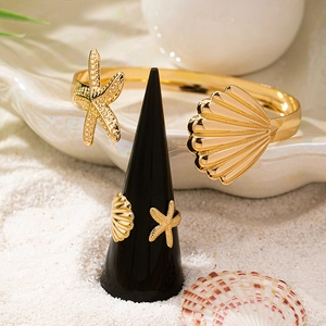 Gold starfish and seashell jewelry set featuring an open bangle and ring on white sand