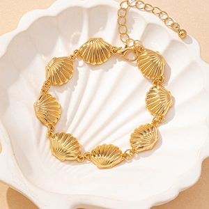 Golden shell charm bracelet and necklace set displayed on a white ceramic shell tray