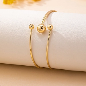 Minimalist gold open wrap bracelet with polished beads on a white textured stand