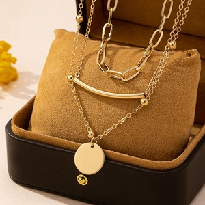 Three-layer layered gold necklace with curb chain and round pendant on display pillow