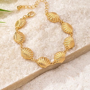 Detailed view of a gold shell bracelet with scallop pendants on a textured stone surface