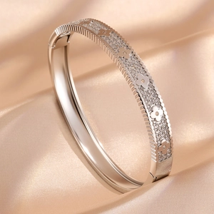 Luxe silver-toned four-leaf clover bangle with pavé-set crystals on elegant silk background