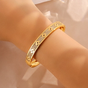 Macro view of gold plated clover bangle featuring pavé crystals and brushed metal texture