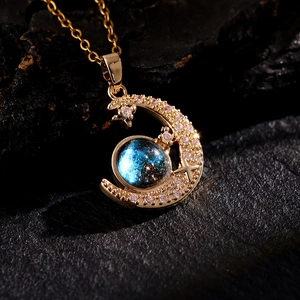 Detail of gold crescent moon pendant featuring sparkling crystals and blue starry stone