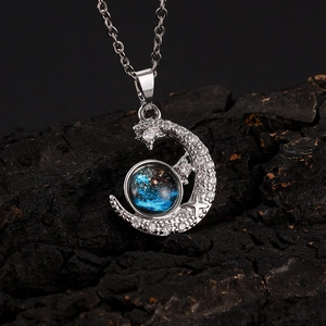 Detailed close-up of silver crescent moon pendant with blue starry galaxy bead on dark stone