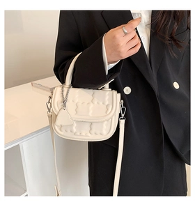 Detail of white quilted half-moon bag featuring a metal heart charm and leather handle