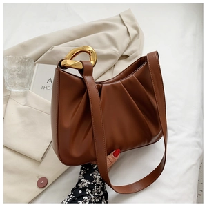 Close-up of brown pleated cloud bucket bag with gold circular metal handle on a beige blazer