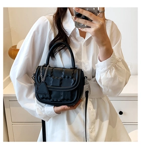 Detail of black quilted crossbody bag with bubble texture and silver chain heart charm